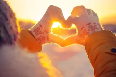 Someone making a heart shape with their golved hands during a winter sunset.