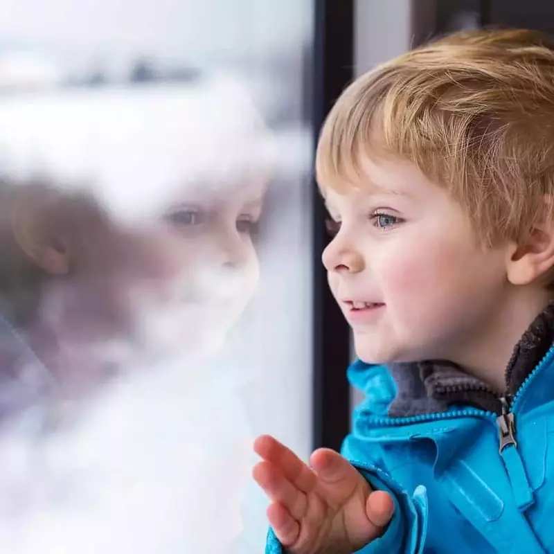 Young boy looking out the window at the snow