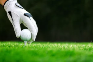 Gloved hand putting a golf ball on a tee.